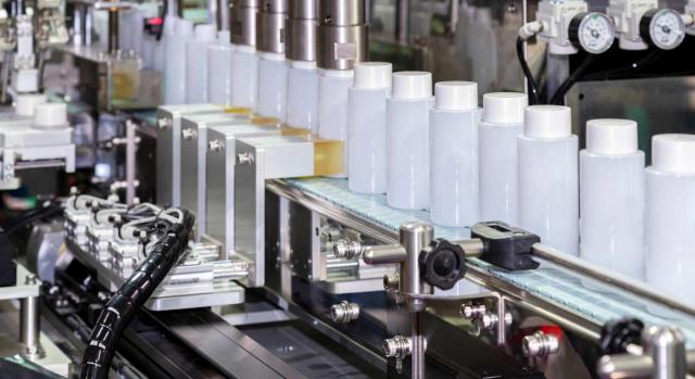 Liquidación del ICIO por la ampliación de la superficie de una fábrica de cosméticos y colocación de todo el equipo industrial. Imagen de máquina de tapado y etiquetado de botellas de plástico en una fábrica