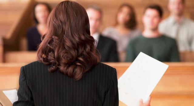 Sujeción al IVA del servicio prestado por un abogado gratuitamente si la parte contraria en caso de ser condenada debe pagar también sus honorarios Es una prestación de servicios a título oneroso a efectos de IVA la representación en juicio por un abogado gratuitamente si en caso de ser condenada en costas la parte contraria  también debe pagar al abogado sus honorarios. Imagen de una abogado exponiendo sus documentos al jurado