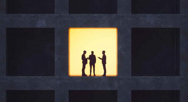 Imagen de un edificio de oficinas, una de ellas con la luz encendida donde se ve la silueta de tres personas hablando sobre el acuerdo de despedido