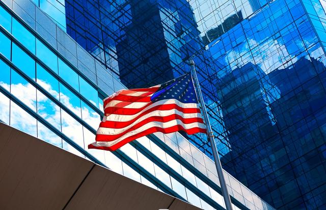 Exceso de retenciones IRNR: grupo trust estadounidense exento Denegación de la devolución de retenciones por IRNR a un grupo trust estadounidense exento de impuestos: exigencia de acreditar también la residencia de los beneficiarios, no solo de las entidades. Imagen de la bandera de EEUU bajo unos rascacielos