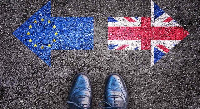 Brexit transición Brexit transición. Banderas con forma de flecha de la comunidad europea e inglesa dibujadas en el asfalto apuntando direcciones opuestas y unos zapatos de caballero en medio