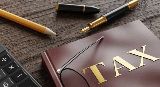 El TEAC anula sanción por no concurrir el elemento subjetivo en el obligado tributario, dada su interpretación razonable de la norma basada en un criterio del tribunal que se modificó con posterioridad. Imagen de un escritorio con una calculadora, un libro de TAX y un boli y lápiz