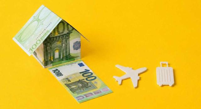Aprobación del impuesto sobre estancias turísticas en Álava. Imagen de una casa hecha de billetes de 100 junto a un avión y una maleta