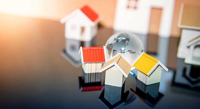 En IRNR se pueden minorar las amortizaciones deducibles del valor de adquisición de un inmueble que estuvo alquilado previamente, pero no se puede duplicar el coeficiente mínimo por ser un bien usado. Imagen de unas casitas pequeñitas sobre un escritorio con tejados de colores