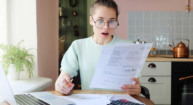 No puede liquidarse como donación la aceptación de una herencia prescrita y renunciada cuando el patrimonio del causante está totalmente absorbido por una deuda firme y ejecutable. Imagen de una chica estando en su cocina mirando con asombro facturas