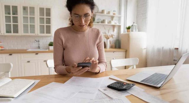 Campaña renta 2021 . Mujer usa el móvil y un portátil para llevar la contabilidad en su casa