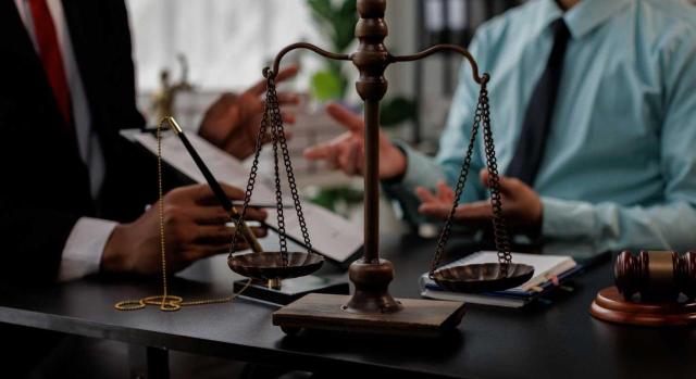 El TS determinará si resulta aplicable el principio ne bis in idem, en su vertiente procedimental, al segundo procedimiento de derivación de responsabilidad subsidiaria. Imagen de una balanza de juicio sobre una mesa de trabajo entre dos hombres