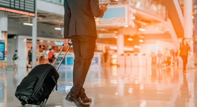 Cálculo de los rendimientos devengados durante los días de estancia en el extranjero que no se corresponden con retribuciones específicas. Hombre de negocios con equipaje de mano caminando en la terminal del aeropuerto