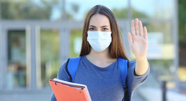 Coronavirus león medidas. Estudiante con mascarillas haciendo stop con la mano