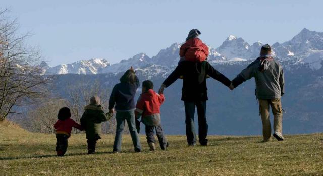 Una familia, de espaldas, con niños cogidos de la mano en el campo miran las montañas nevadas