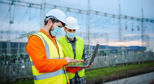 Se prorrogan medidas en materia de fiscalidad energética y del tipo impositivo del IVA de productos para combatir la COVID-19 (RDL 29/2021). Imagen de dos obreros mirando un ordenador portátil