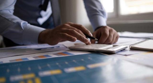 Proyecto de Orden: relación de valores negociados en centros de negociación, con su valor de negociación medio correspondiente al cuarto trimestre de 2025, a efectos de la declaración del IP de 2025 y del modelo 189. Imagen de un hombre haciendo cuenta con una calculadora sobre unos gráficos