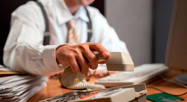 La escritura que documenta la cesión o transmisión de una oficina de expendeduría de tabaco y timbre del Estado está sujeta a AJD La escritura que documenta la cesión o transmisión de una oficina de expendeduría de tabaco y timbre del Estado está sujeta a AJD al ser inscribible en el Registro de Bienes Muebles. Imagen de un hombre trabajando mientras cuelga el telefono de hace unos cuantos años