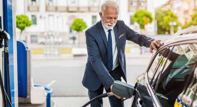 Calificación en el IRPF de las retribuciones percibidas por socios que prestan servicios en sociedades, incluyendo la consideración de cuotas de autónomo asumidas por la empresa y el tratamiento de los gastos de desplazamiento y gasolina. Imagen de un hombre mayor trajeado hechando gasolina a su coche