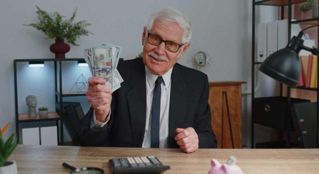 Deducibilidad en el IS de una retribución vitalicia al antiguo administrador tras su jubilación. Imagen de un señor mayor trajeado con muchos billetes en la mano