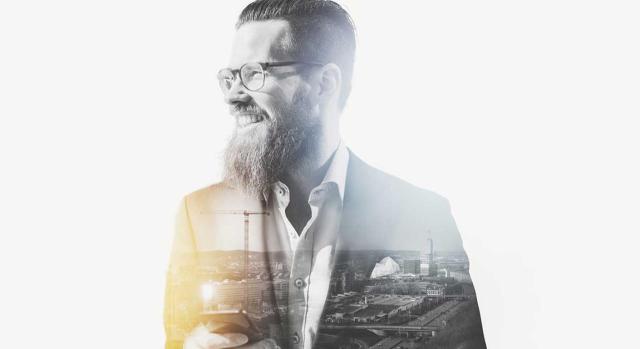 Requisitos subjetivo para aplicar régimen de fusiones: 2 sociedades 1 único socio Operación de fusión por absorción en IS entre dos sociedades participadas íntegramente por el mismo socio. Imagen de un hombre con movil en la mano y la ciudad de fondo