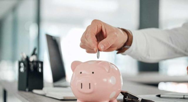 Criterios de prueba en ingresos en efectivo y ahorros para el IRPF, fraccionamiento de ingresos como indicio de ocultación fiscal. Imagen de una persona hechando una moneda en un cerdito rosa encima de un escritorio