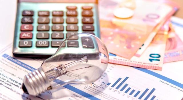Repercusión del tipo impositivo del Impuesto sobre la Electricidad y control de los tipos mínmos del art. 99.2 Ley Impuesto Especiales. Imagen de bombilla, calculadora y dinero en efectivo