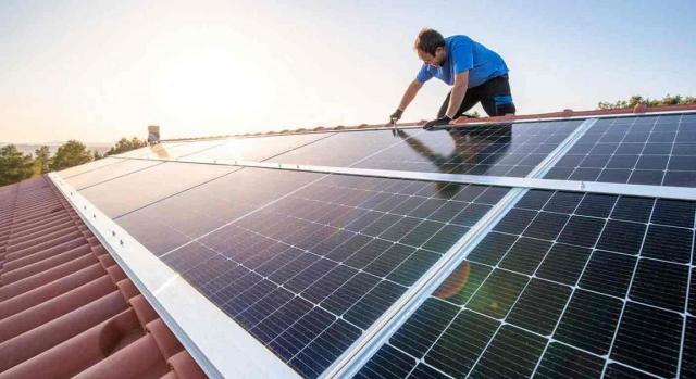 IRPF, deducciones mejora eficiencia energética viviendas. Imagen de un trabajador profesional instalando paneles solares en el techo de una casa