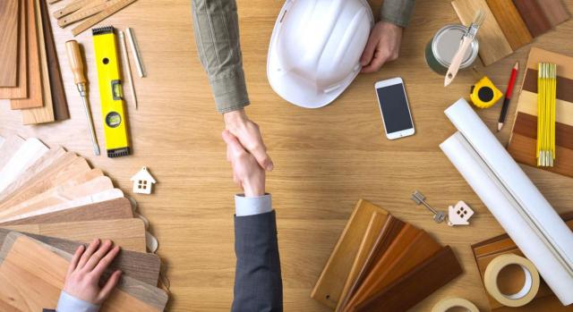 Tipo del 10% de IVA para inquilinos que rehabilitan la vivienda Obras de rehabilitación realizadas por los inquilinos como pago en especie del alquiler a efectos del tipo reducido del IVA. Imagen de dos manos cogiendose sobre una mesa de arquitectos con material de trabajo