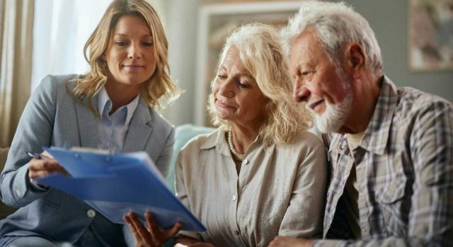 El exceso producido en la liquidación de la sociedad conyugal y compensado con un bien privativo queda comprendido en el supuesto de exención objetiva prevista para la sociedad de gananciales. Imagen de una pareja senior que está siendo ayudada por una joven en tema de papeleo