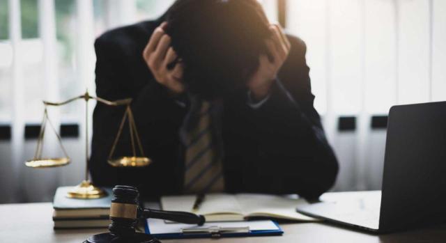 A efectos de estimar la concurrencia o no de una reformatio in peius es suficiente comprobar que el resultado final de la nueva liquidación no supere al de la inicialmente dictada y anulada. Imagen de un joven con gesto de preocupación sobre una mesa de trabajo con la balanza y el mazo de juez