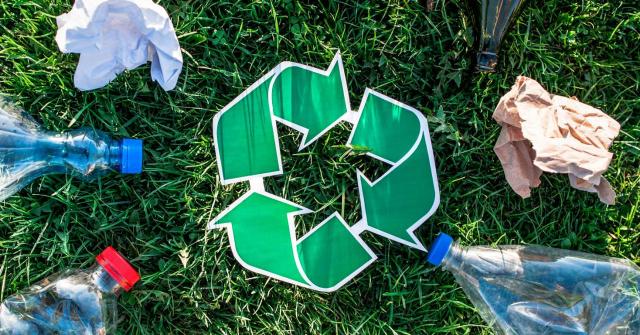 El Tribunal Supremo admite a trámite los recursos del Ayuntamiento de Madrid contra las sentencias que anularon la tasa de basuras. Imagen del logo de reciclaje en un cesped rodeado de botellas de plastico y cristal y papeles