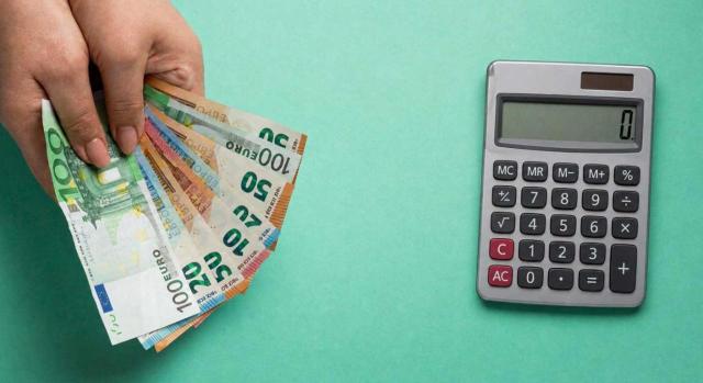 IP exención de participaciones en entidades: cómputo de beneficios atribuidos por una entidad transparente para valorar el cumplimiento del requisito de rendimientos por funciones directivas IP exención de participaciones en entidades: cómputo de beneficios atribuidos por una entidad transparente para valorar el cumplimiento del requisito de rendimientos por funciones directivas. Imagen de una mano con billetes y una calculadora sobre fondo verde