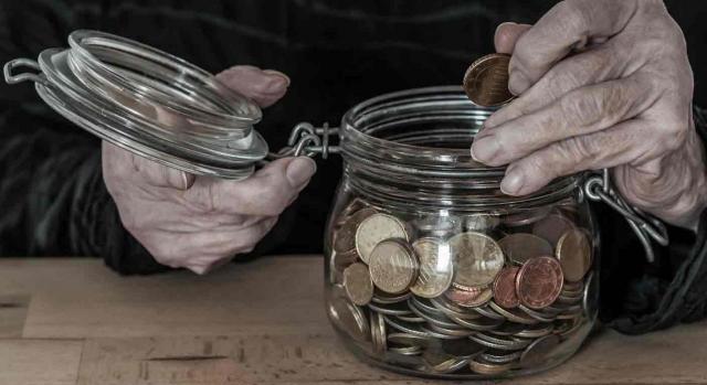 Modificación reglamentos previsión social Modificación reglamentos previsión social. Manos de un anciano metiendo una moneda en un tarro de cristal medio lleno