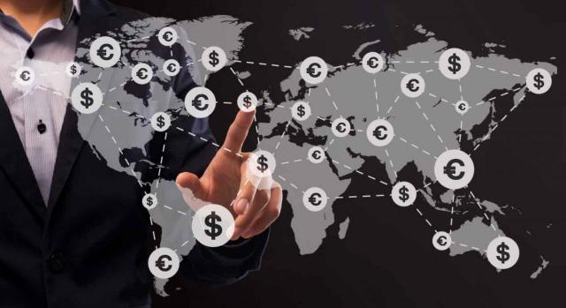 Asimetrías fiscales 2016/1164. Empresario señala con el dedo un lugar en el mapa del mundo sobre el que aparecen iconos de divisas