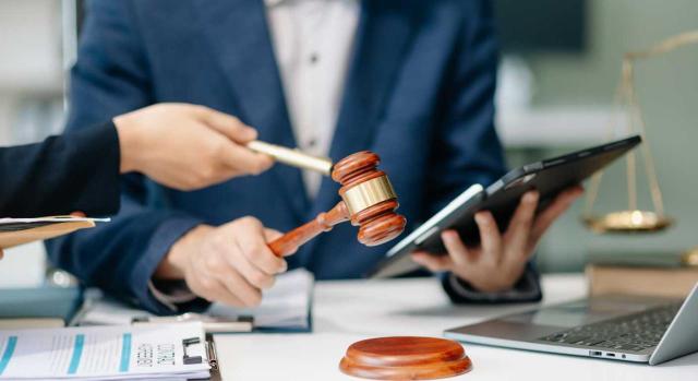 No cabe la impugnación en vía económico-administrativa de los actos de adjudicación de bienes embargados, al tener el acta de adjudicación naturaleza de documento público de venta. Imagen de dos personas sentadas en la mesa donde hay una maza de juez, la balanza y un ordenador portátil