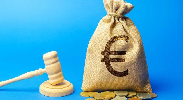 TEAC: desestima que una entidad pueda deducir como gasto, aplicada la deducción por doble imposición internacional, los intereses de un préstamo concedido a una filial extranjera, porque no realiza una actividad económica en el extranjero. Imagen de un mazo de juez al lado de un saco con el símbolo del dollar y monedas