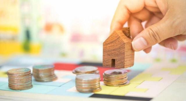 El periodo de generación del incremento de valor a efectos del IIVTNU no se altera en el caso de que el terreno adquiera el carácter urbano durante el mismo, iniciándose en el momento de su adquisición y no cuando adquiere el carácter urbano. Imagen de una casita sujetada por una mano con dinero a su alrededor