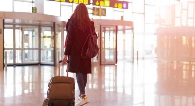 Régimen especial de tributación por el IRNR para trabajadores desplazados a territorio español Régimen especial de tributación por el IRNR para trabajadores desplazados a territorio español. Vista trasera de mujer saliendo del aeropuerto con equipaje de mano