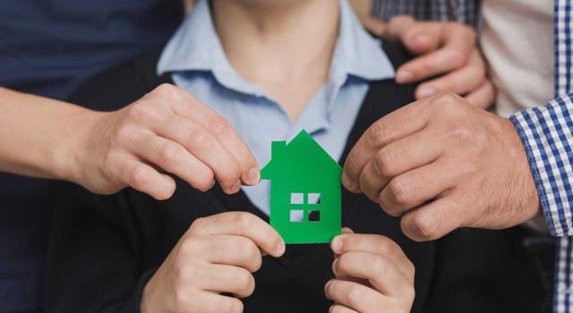 El TSJ de Andalucía resuelve que la reducción por adquisición de vivienda habitual del causante corresponde en exclusiva a su adjudicatario. Imagen de una mujer sujetando la imagen de una casa verde junto a otras personas