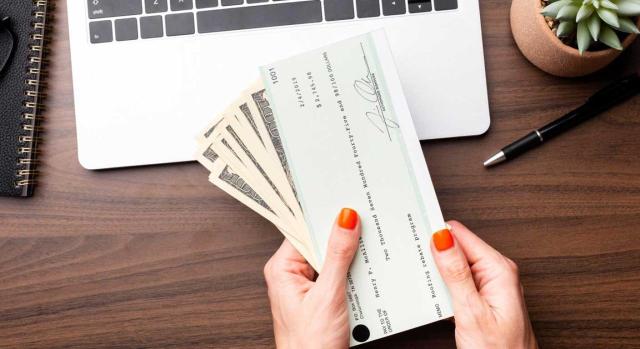 Ganancia patrimonial no justificada derivada del cobro de cheques y pagarés al portador o bien a nombre del contribuyente procedentes de servicios ficticios a sociedades. Imagen de la mano de una mujer en la que tiene un cheque y billetes entre sus dedos