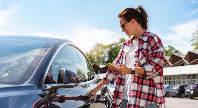 DGT: los automóviles a cuantificar en el IAE serán todos los que estén afectos a la actividad de alquiler de vehículos y de los que disponga el titular por cualquier clase de título, no solo propiedad. Imagen de una mujer desbloqueando su coche con el móvil