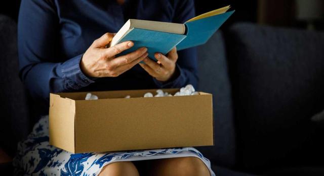 El TJUE estima que puede constituir una restricción a la libre circulación de mercancías establecer una tarifa mínima por el servicio de entrega de libros a domicilio. Imagen de una mujer sentada sacando un libro de una caja y leyendo las primeras hojas
