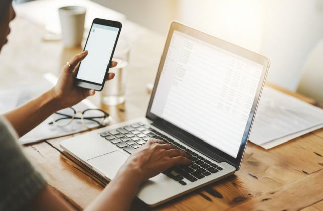 Un móvil o un ordenador puede considerarse gasto deducible en IRPF si se demuestra su afectación exclusiva a la actividad. Mujer en mesa con ordenador y movil en la mano