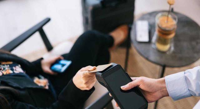 IVA reducido en hoteles: alojamiento y tratamiento de otras prestaciones accesorias según normativa interna. Imagen de una mujer pagando con datafono en un comercio
