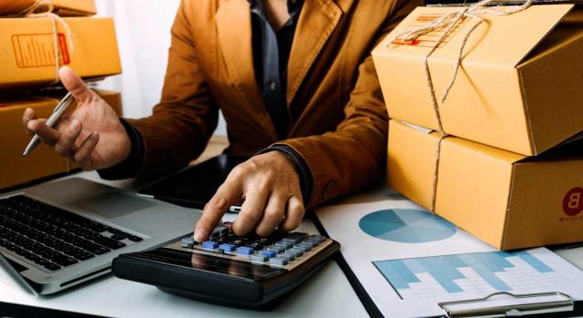 TEAC: cambio de criterio respecto a la DGT respecto al régimen de diferimiento del IVA a la importación Diferimiento del IVA a la importación: el TEAC fija, de forma contraria a la DGT, que el requisito del período de liquidación mensual debe cumplirse en el ejercicio de efectos de la opción, y no cuando se ejercita formalmente la opción en noviembre. Imagen de un hombre haciendo cuentas sobre el precio de paquetería