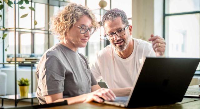 Exención en el Impuesto sobre el Patrimonio de las participaciones en una entidad dedicada al alquiler de inmuebles, aunque la empleada sea la esposa del propietario del 99,9% del capital. Imagen de una pareja en su casa haciendo gestiones con el ordenador