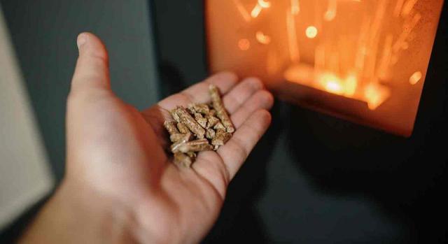 IVA gas natural. Pellet sobre una mano y detrás una chimenea encendida