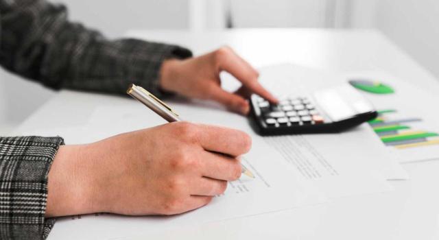 IVA: la regularización de cuotas indebidamente facturadas en un periodo objeto de un control fiscal concluido puede quedar supeditada a la presentación de nuevos elementos. Imagen de las mandos de una persona haciendo cuentas con una calculadora sobre papel y gráficas