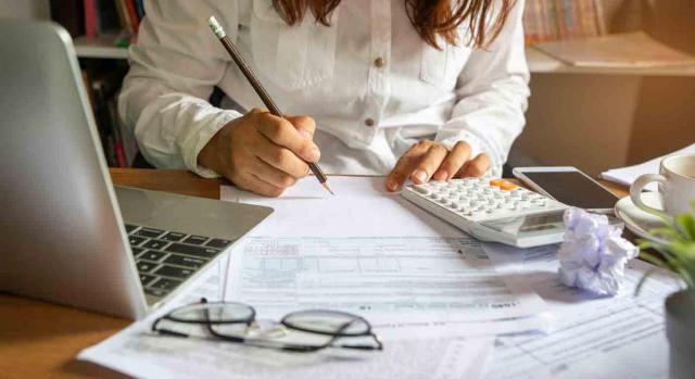 Recomendaciones, ahorro, IRPF, 2020. Mujer haciendo cálculos sobre una mesa con una calculadora, unas hojas y un portátil