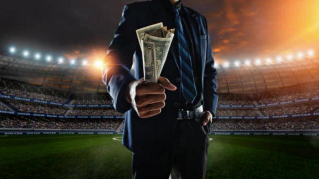 El Real Madrid no puede deducirse el IVA de los agentes de los futbolistas. Imagen de ejecutivo en pie sobre el campo de futbol con dinero en efectivo en la mano