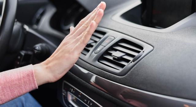 No está sujeta al impuesto sobre los gases fluorados de la importación de estos gases en los equipos de refrigeración de un vehículo No está sujeta al impuesto sobre los gases fluorados de la importación de estos gases en los equipos de refrigeración de un vehículo. Mano de mujer frente a la rejilla de ventilación del aire acondicionado en el coche