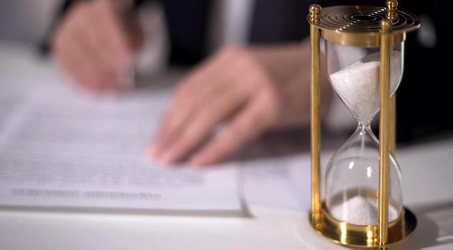 Impacto del concurso de acreedores y la calificación de concurso fortuito en la responsabilidad subsidiaria del administrador Impacto del concurso de acreedores y la calificación de concurso fortuito en la responsabilidad subsidiaria del administrador. Imagen de un hombre firmando algo con un reloj de arena dorado a su lado