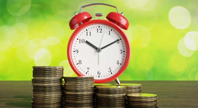 Deducibilidad en la determinación del rendimiento neto de actividades económicas en el IRPF los intereses de demora derivados de actas de inspección del IRPF de años anteriores. Imagen de un reloj despertador rojo y unas monedas delante de él