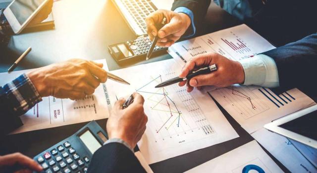 Para aplicar la exención en IAE y mantenerse por debajo del millón de euros, el importe neto de la cifra de negocios debe calcularse de forma agregada, sumando la cifra de negocios de todas las entidades del grupo. Imagen de una mesa de trabajo con trabajadores mirando gráficas